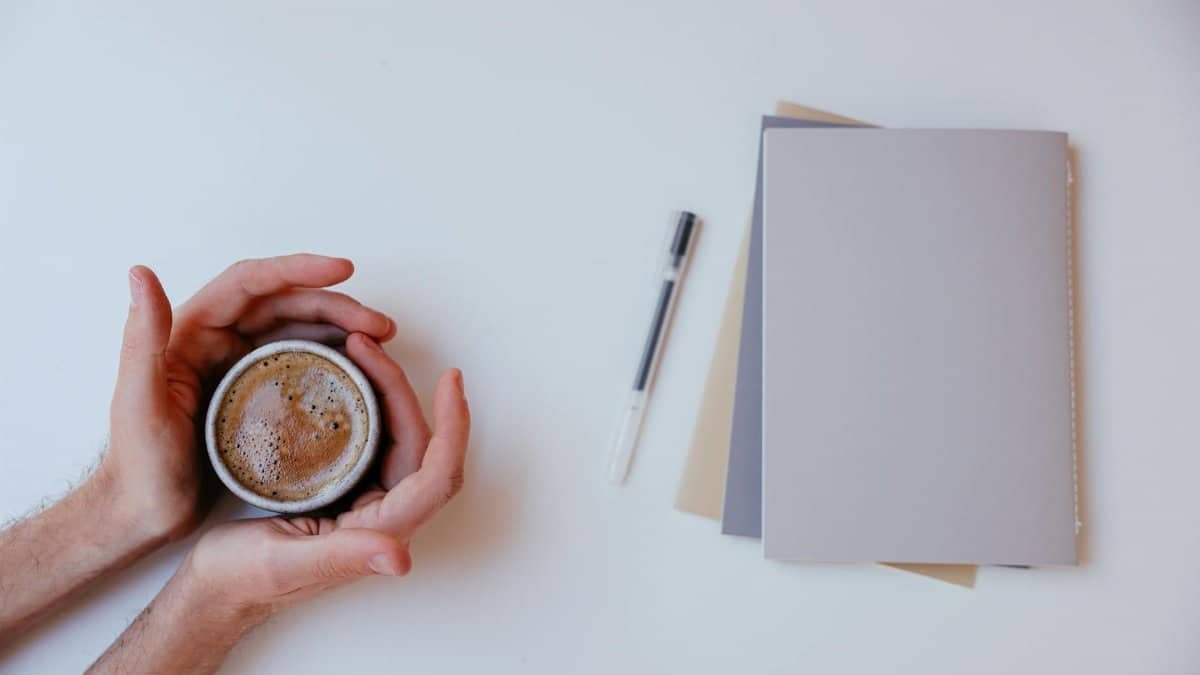 A warm coffee surrounded by notebooks and pen on a white background, perfect for productivity.