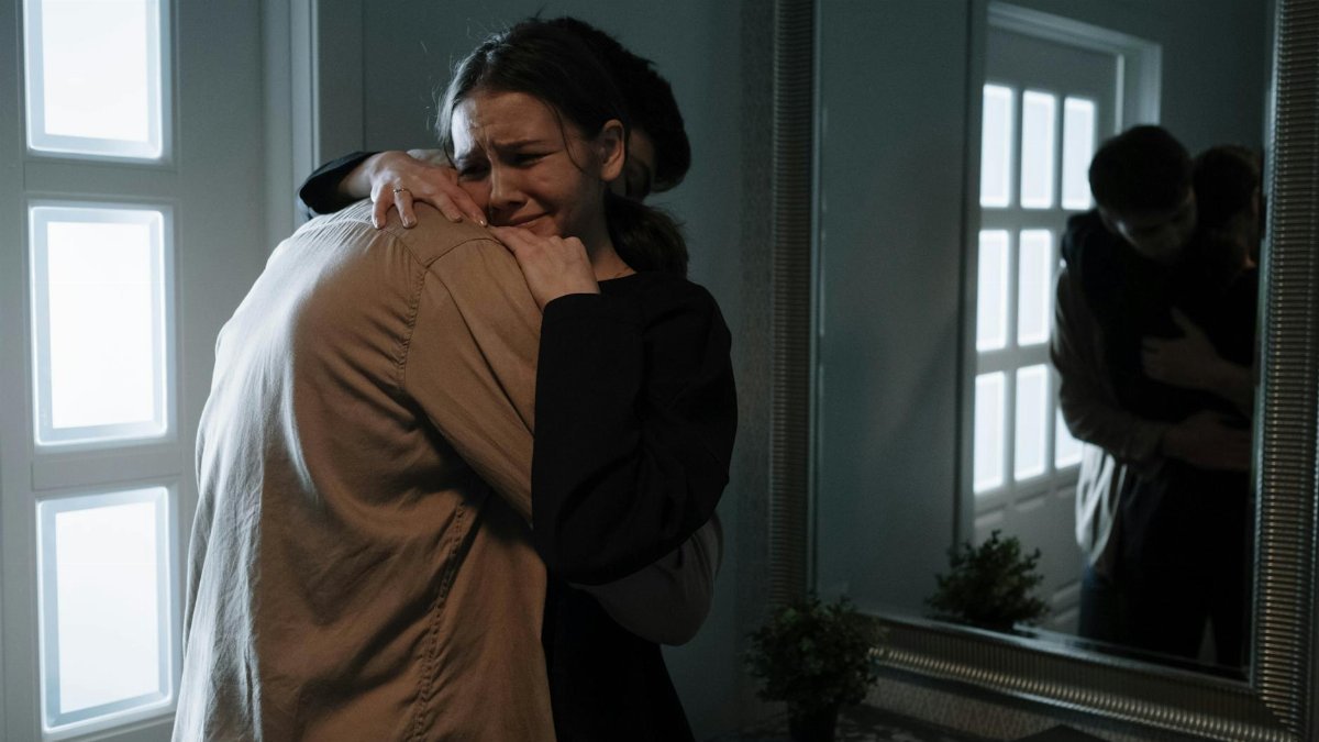 A touching scene of two adults hugging with reflection in mirror, indicating emotional support.