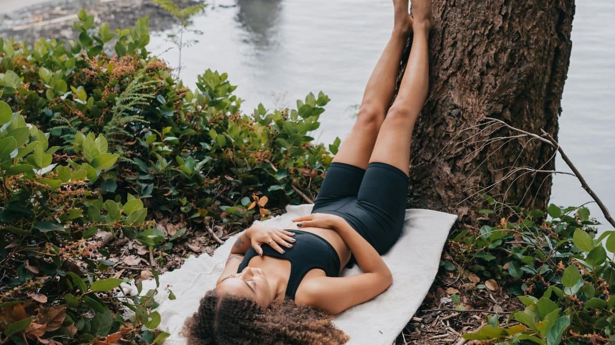 Young woman relaxing on a blanket by a tree near water in nature.