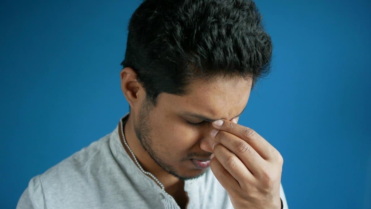 A man showing stress or headache by pinching his nose bridge against a blue backdrop.