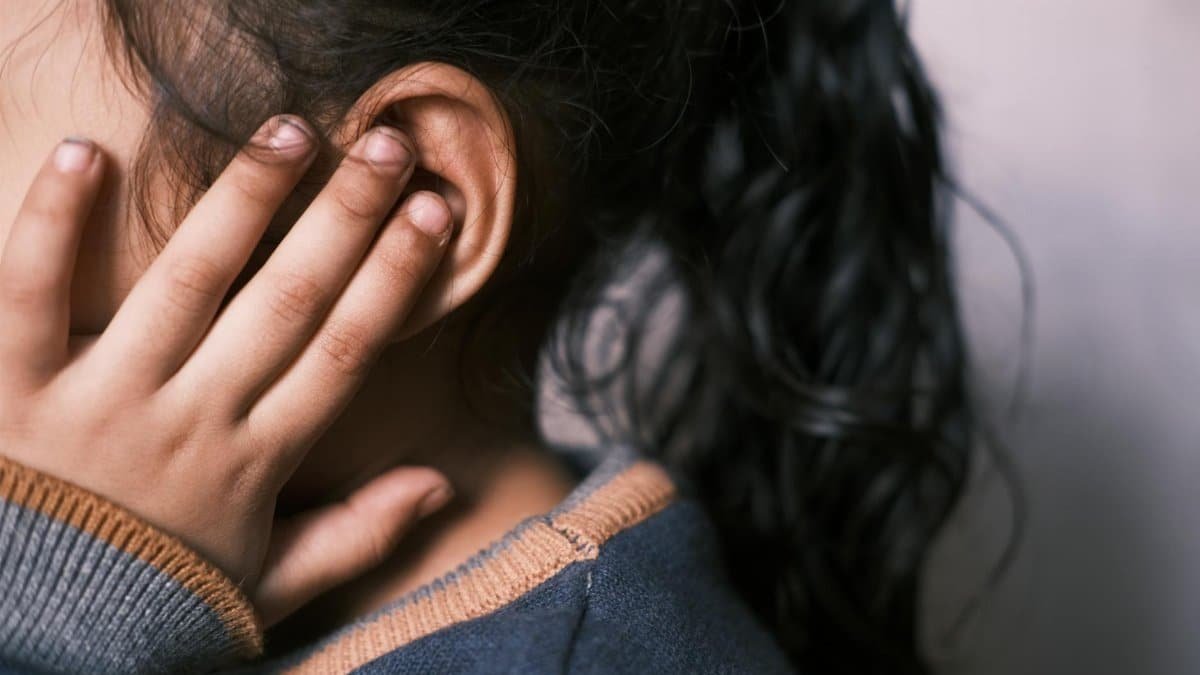 A young girl with long dark hair covering her ear in a thoughtful pose.