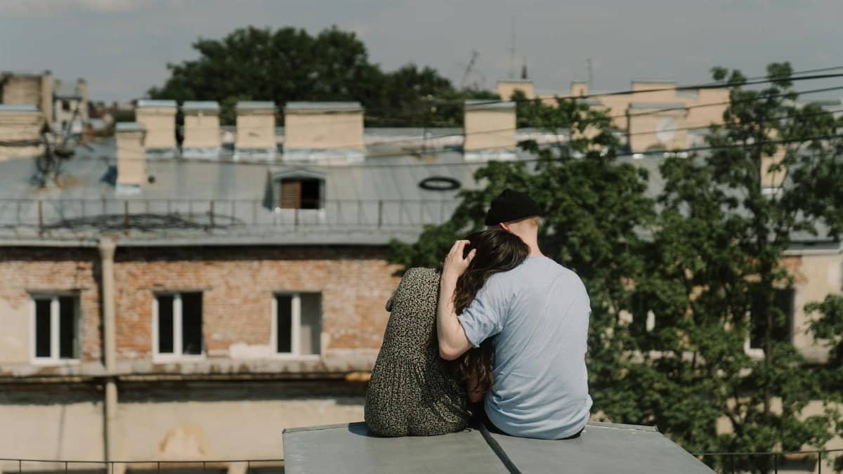 A couple sits on a rooftop, enjoying a romantic moment with a cityscape view.