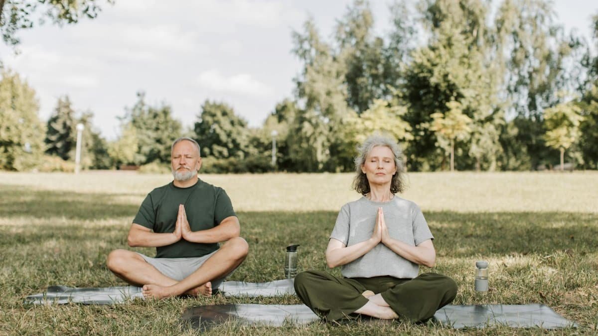 Senior couple meditating on yoga mats in a serene park setting, enjoying peaceful yoga practice.
