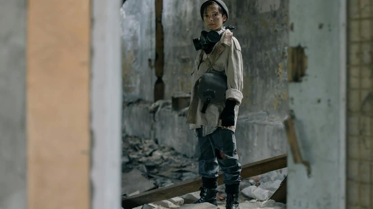 Young person in protective gear stands in a desolate, abandoned building, symbolizing survival.