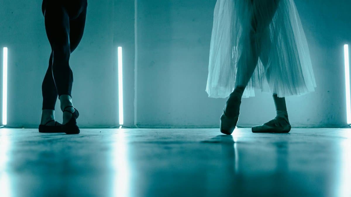 Two ballet dancers pose gracefully in a dimly lit studio, showcasing elegance and poise.