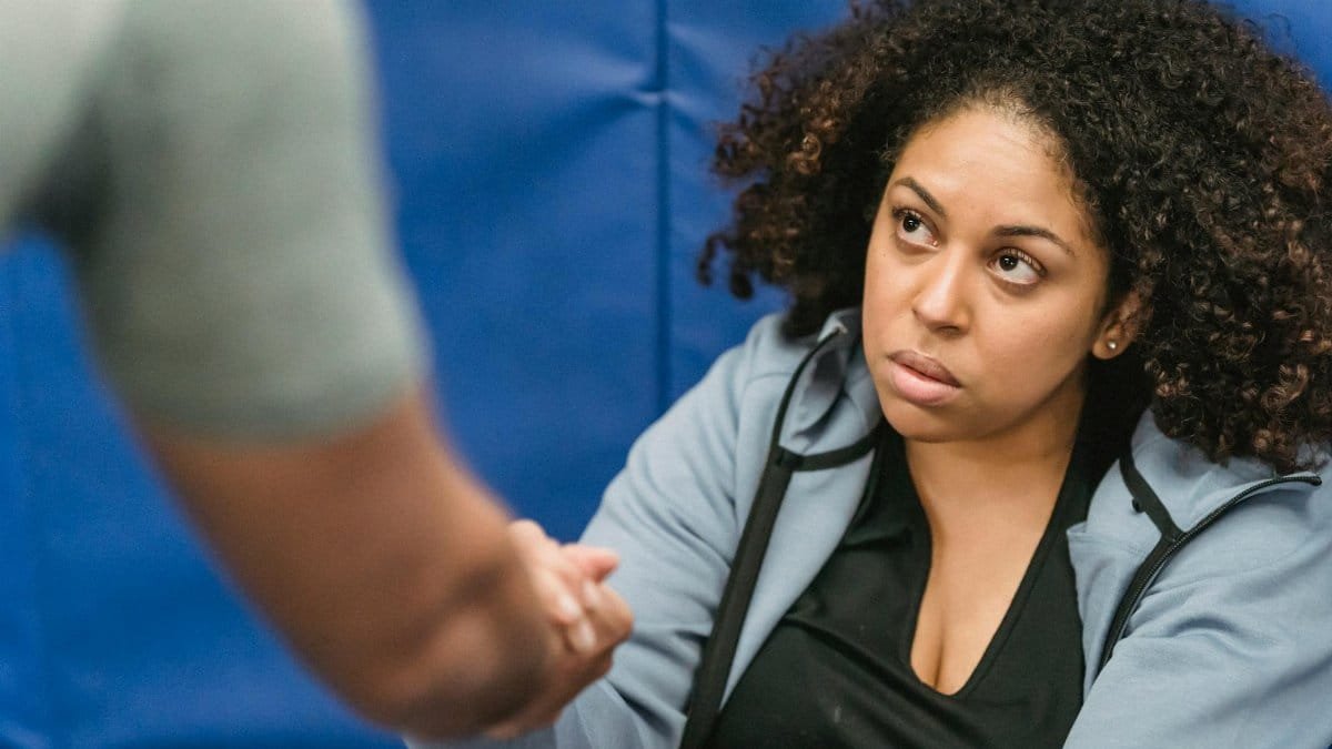 A determined woman receives motivational support in a gym setting, fostering teamwork and resilience.