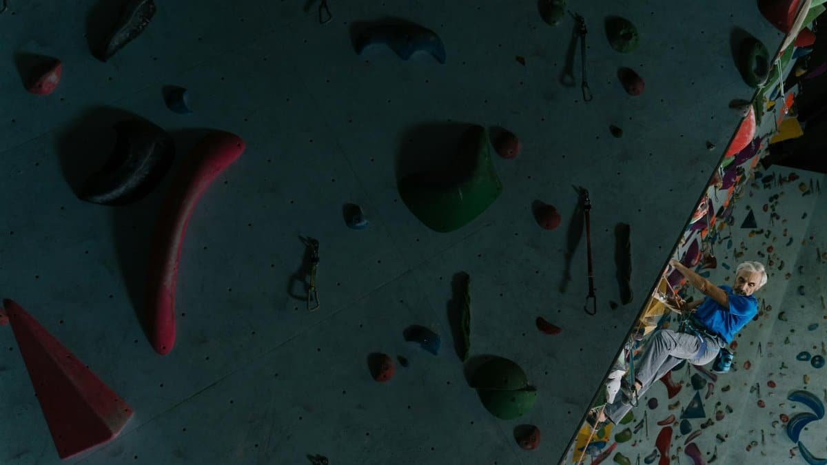 A senior man skillfully climbing an indoor bouldering wall challenges age limits.