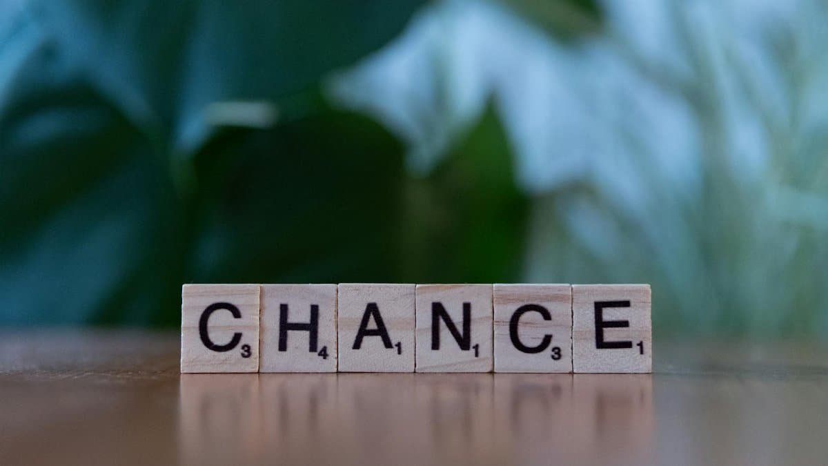 Scrabble tiles spelling 'chance' on a wooden surface with a blurred green background.