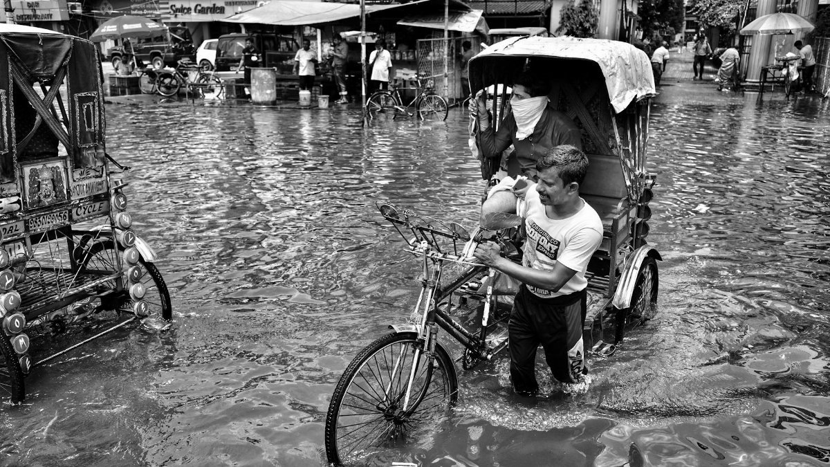 Black and white image of a man pulling a rickshaw through a flooded street in Kolkata, India.