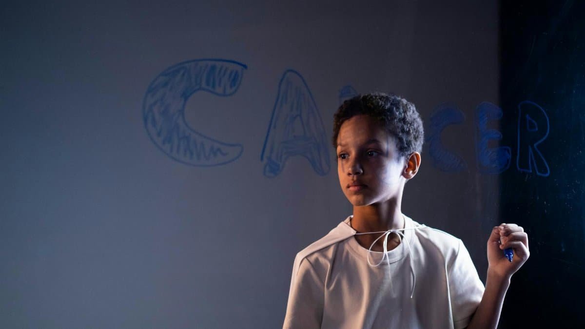A young boy stands indoors holding a marker, raising cancer awareness.
