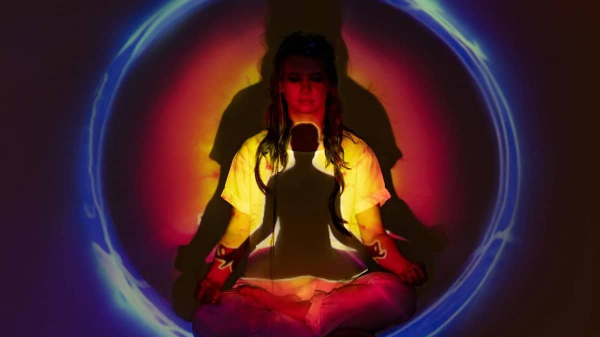 A woman in meditation surrounded by colorful auric light, creating a spiritual atmosphere.
