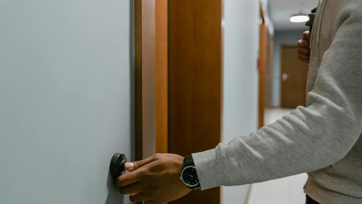 An adult ringing a doorbell in a residential hallway indoors.