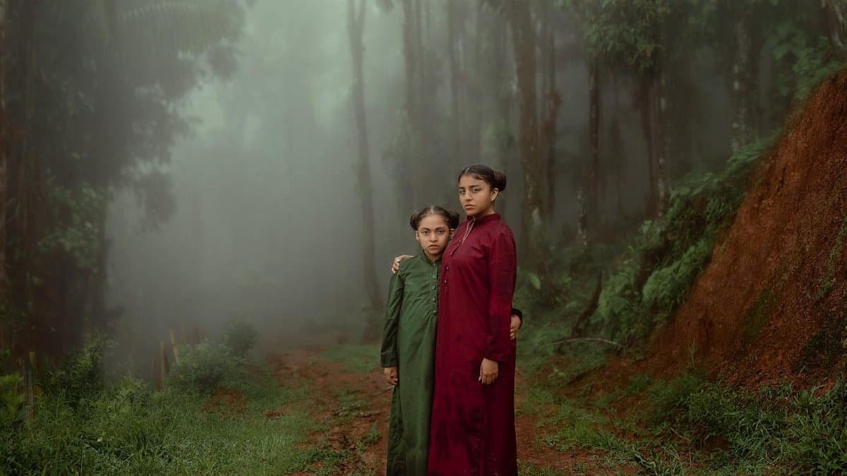 Two sisters embracing on a misty forest path in Tingo María, Peru, creating a serene atmosphere.