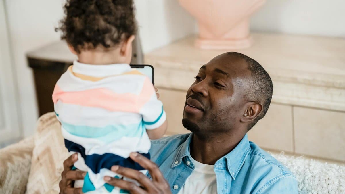 A father holding his young child indoors, sharing a joyful moment at home.