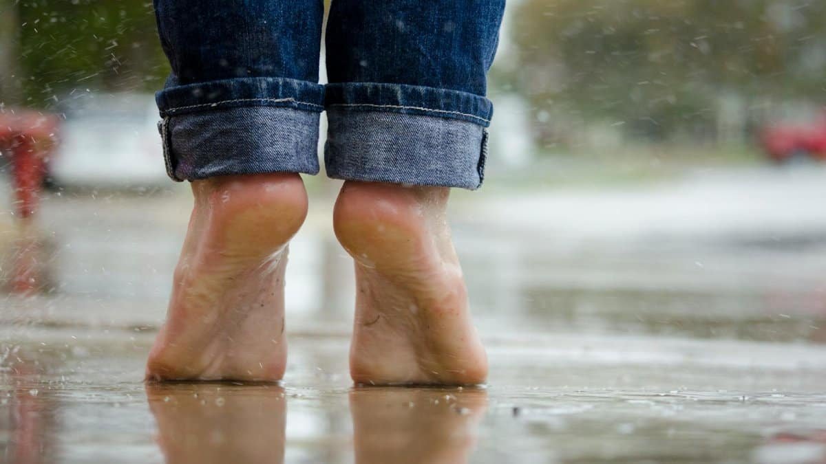 Close-up of bare feet on a wet pavement, capturing calm and connection with nature.