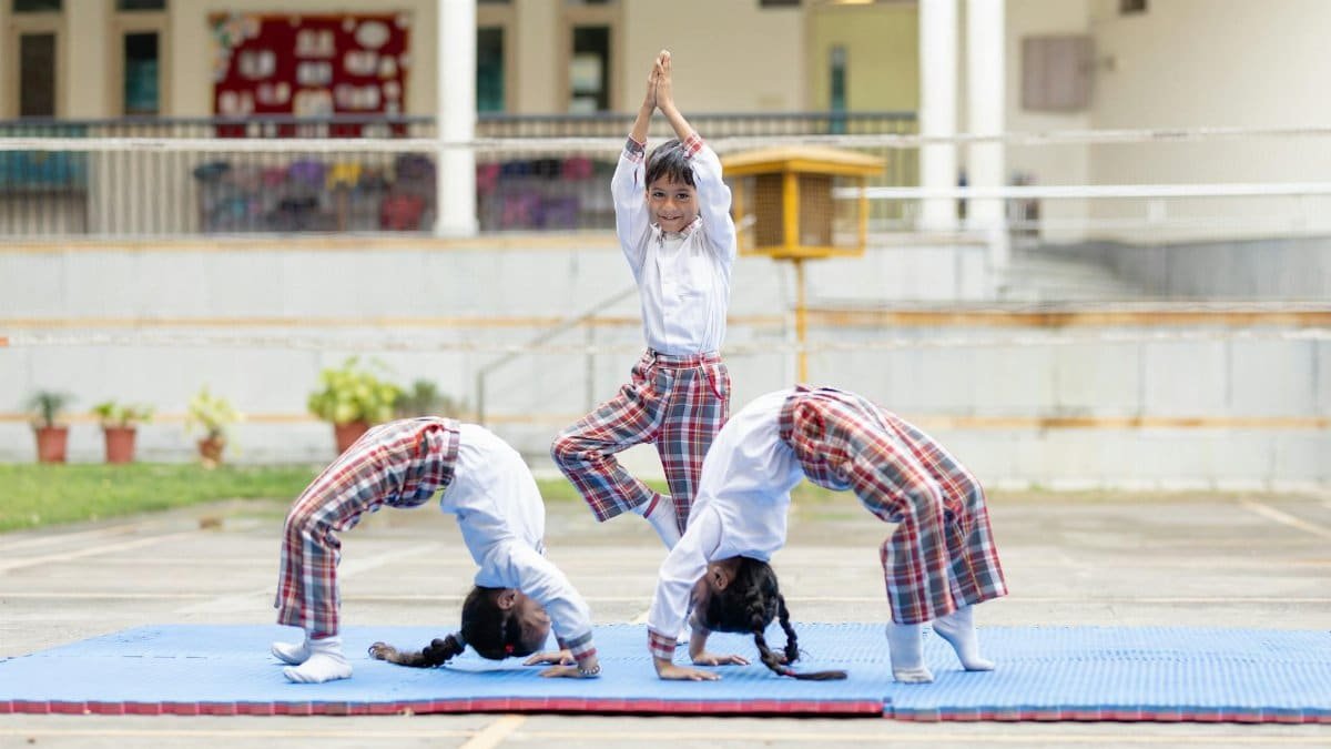 Three children performing yoga poses outdoors on a school playground.