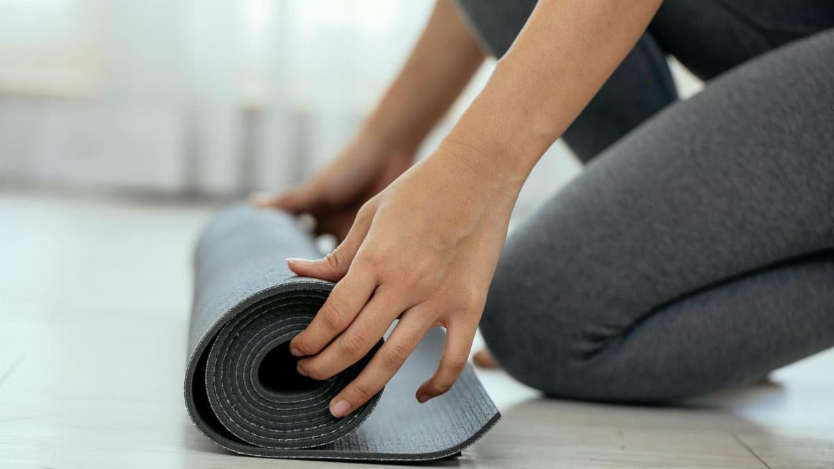 Close-up of a woman rolling out a yoga mat in a bright indoor space, ready for a workout.