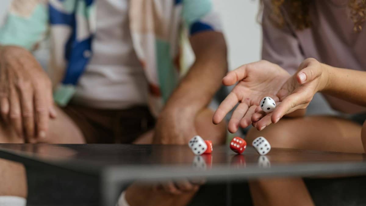 Two people playing a dice game, showcasing hands and rolling dice on a table.
