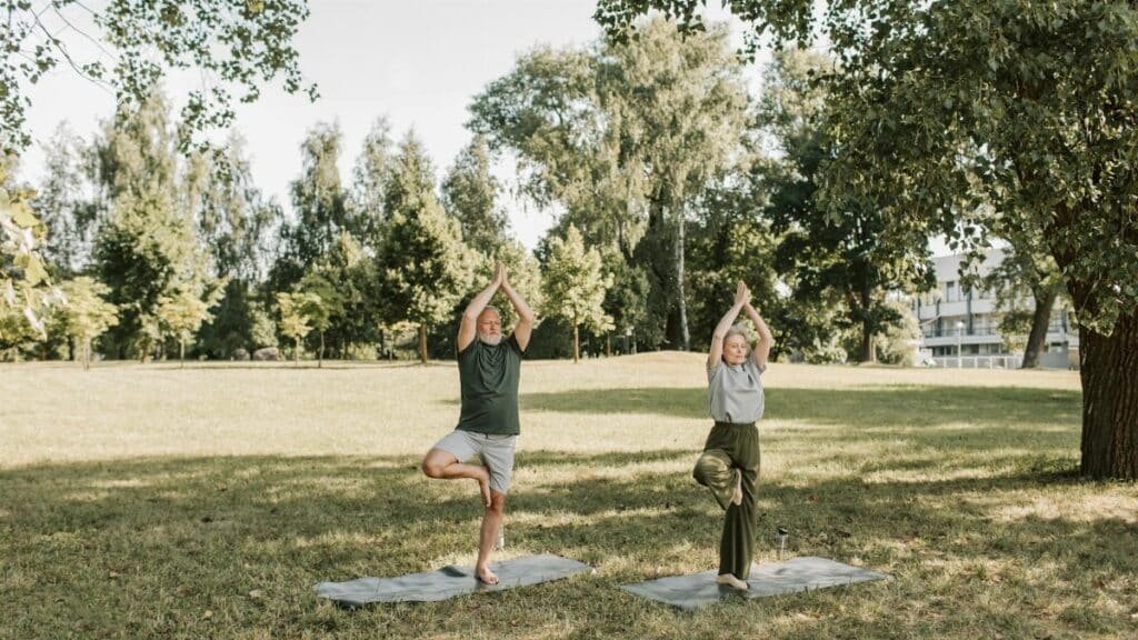 Elderly couple performing yoga in a sunny park, enhancing health and mindfulness.