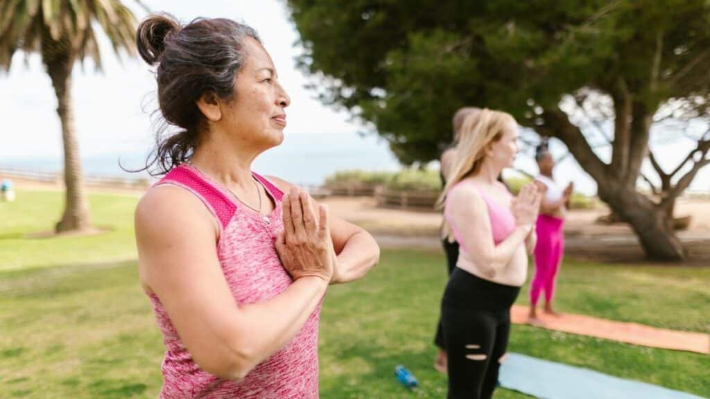 A senior woman practicing yoga with a group in a sunny park, promoting health and relaxation.