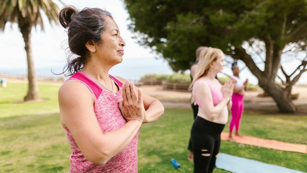 A senior woman practicing yoga with a group in a sunny park, promoting health and relaxation.