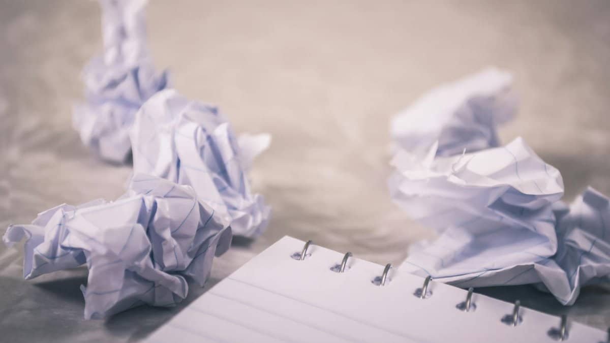 Crumpled papers scattered around a notepad, symbolizing creative process and ideas.