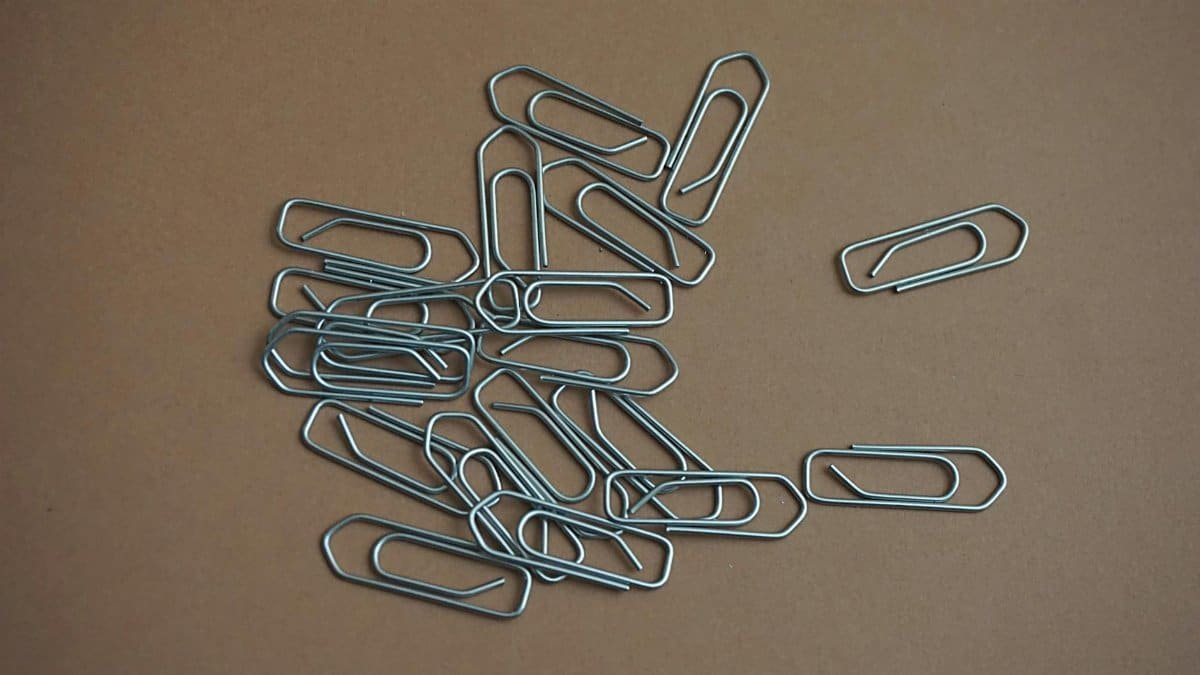 A collection of metal paper clips scattered on a brown surface, showcasing office supplies.