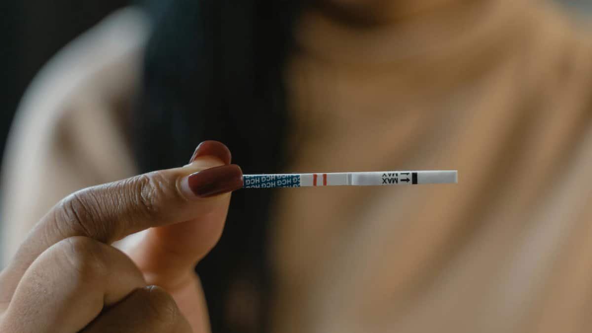 A hand holds a positive pregnancy test strip against a blurred background, symbolizing new beginnings.
