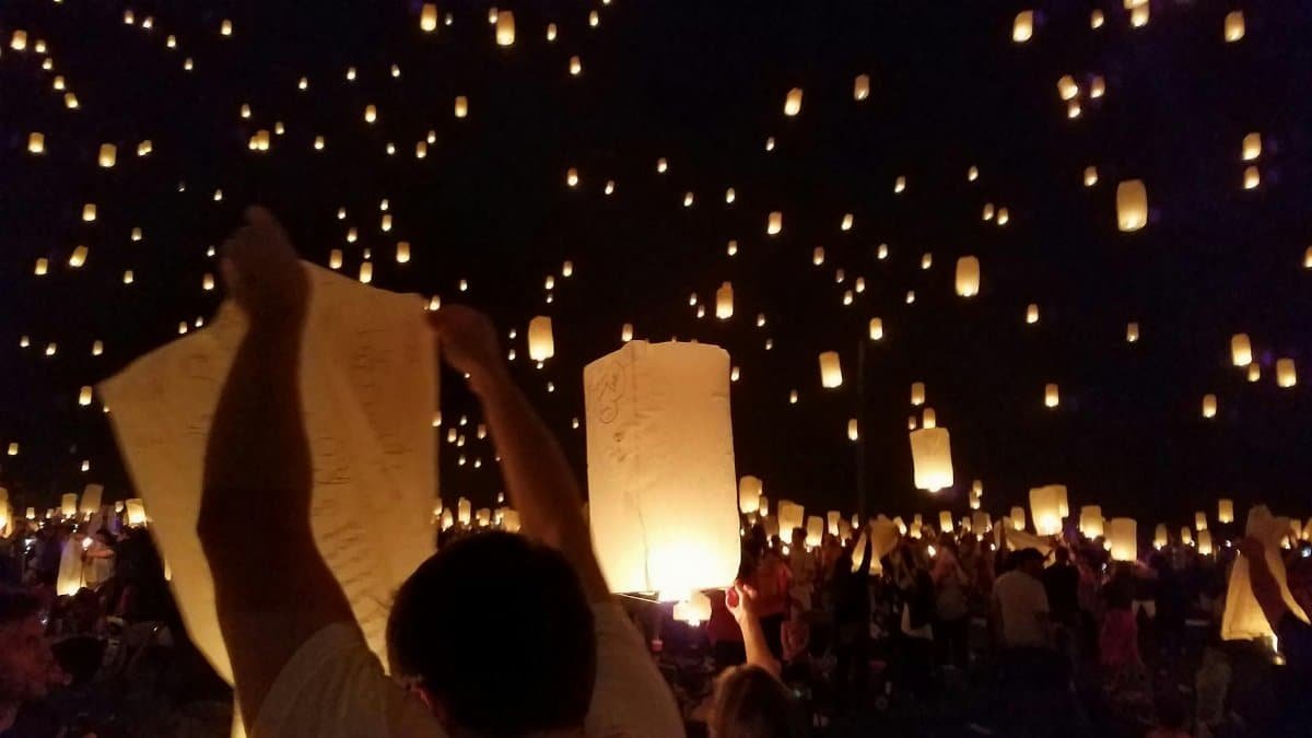 A vibrant night sky filled with glowing sky lanterns during a lively festival.