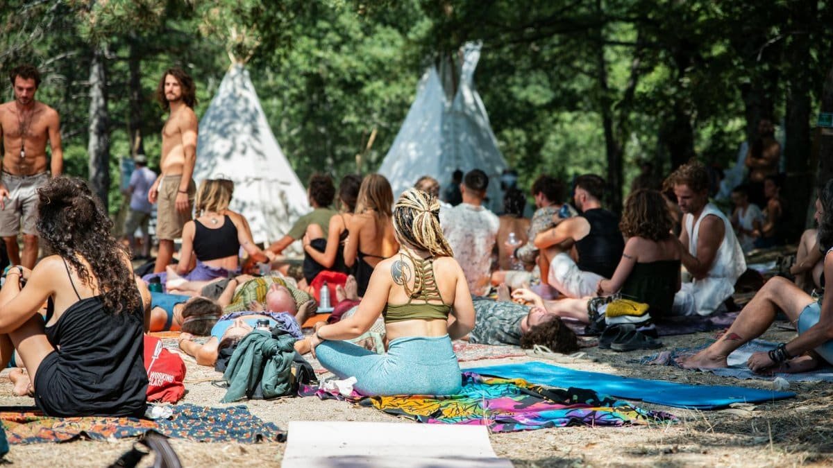A diverse group enjoys a community event in a forest with teepees.