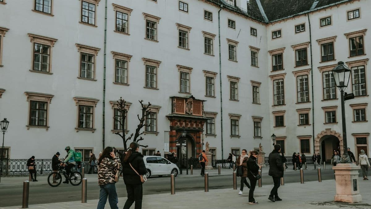 A lively street scene with people walking by a historic building in Vienna, Austria.