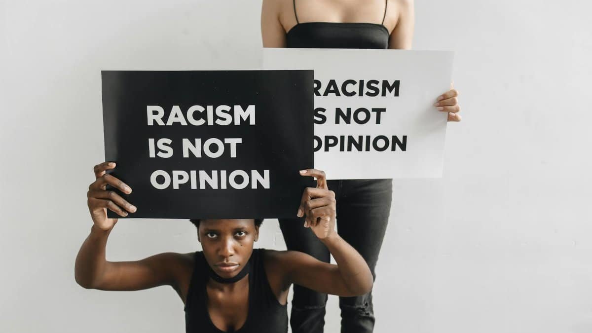 Two women holding signs with anti-racist slogans, emphasizing justice and community support.
