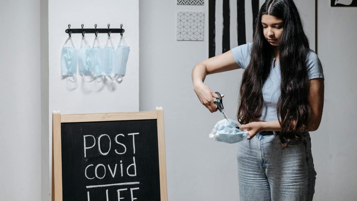 A young woman symbolically cuts a face mask in a post-COVID life setting.