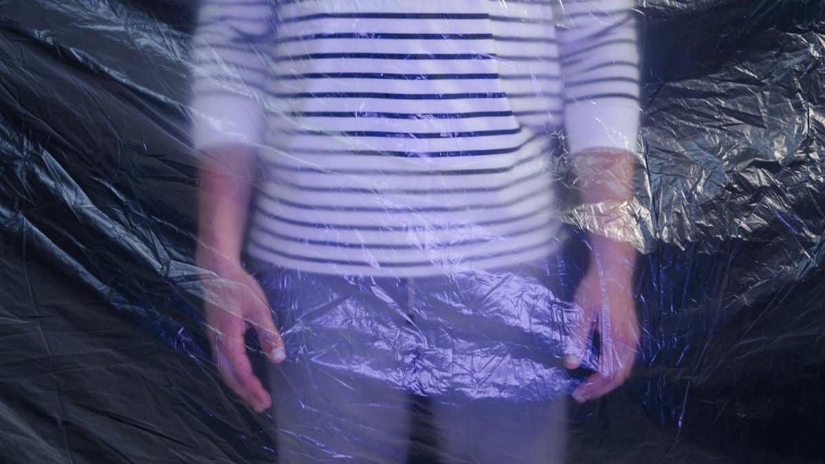 Abstract image of a person in a striped shirt blurred behind semi-transparent plastic.