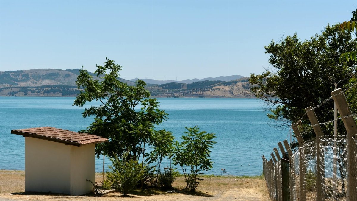 Tranquil lakeside view with trees and a path leading to the water, under a clear sky.