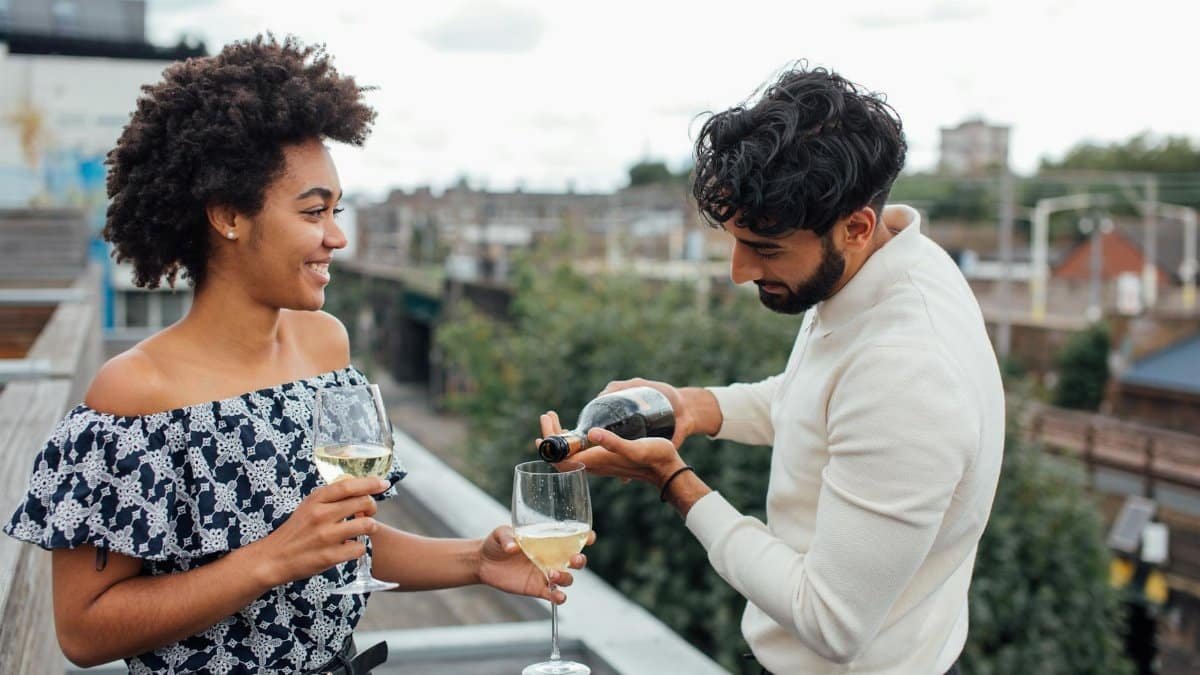 Smiling couple toasting with wine on a rooftop, enjoying a cheerful evening outdoors.