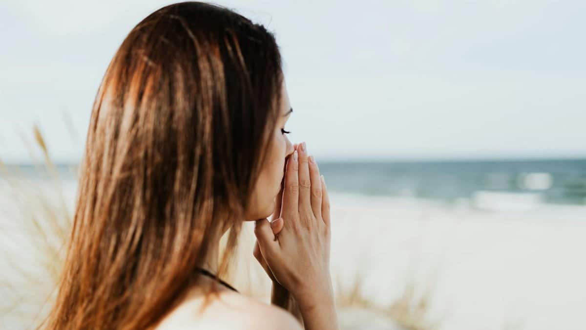 Woman meditating by the beach with hands together, embracing tranquility and peace.