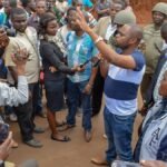 A diverse group discusses community issues with a politician in an outdoor setting.