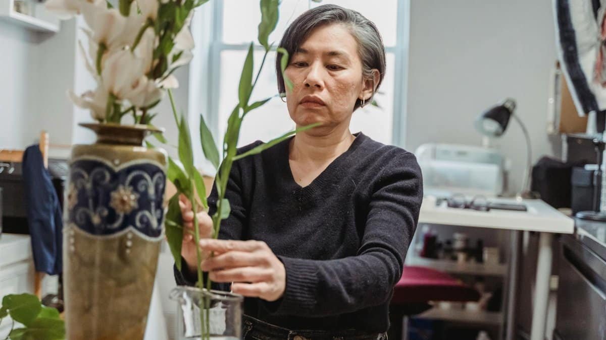 A woman creatively arranging flowers in a vase indoors. Perfect for design and decor themes.