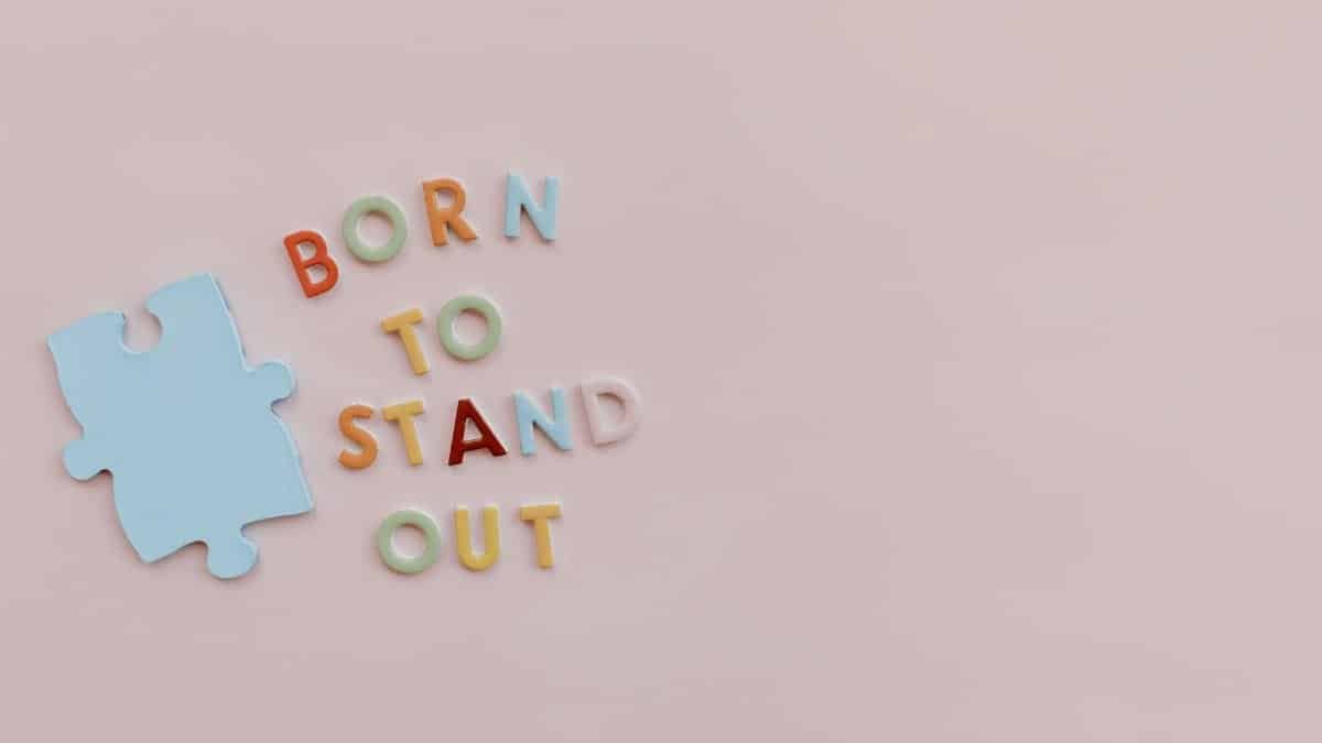 Colorful letters spelling 'Born to Stand Out' with puzzle piece symbolizing autism awareness on pink background.
