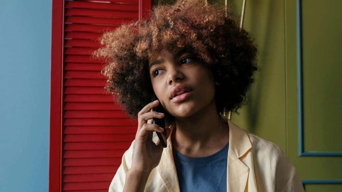 Contemplative woman with curly hair taking a phone call indoors with colorful background.