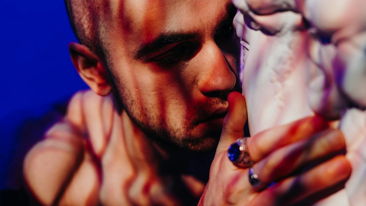 Intimate close-up of a man embracing a sculpture, illuminated by dramatic shadow patterns.