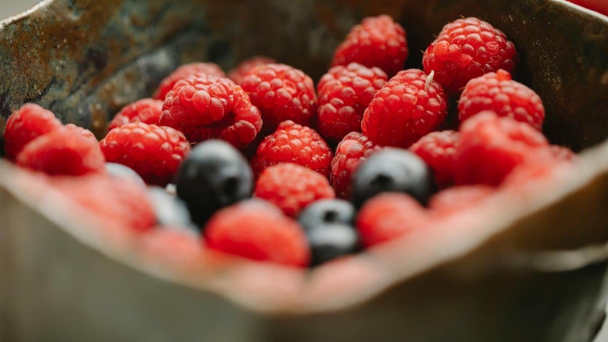 Close-up of fresh raspberries and blueberries in a metal bowl. Vibrant and healthy.