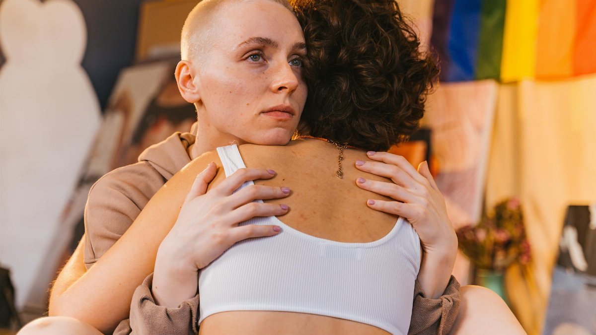 Tender embrace between two women indoors, symbolizing support and connection in a colorful setting.