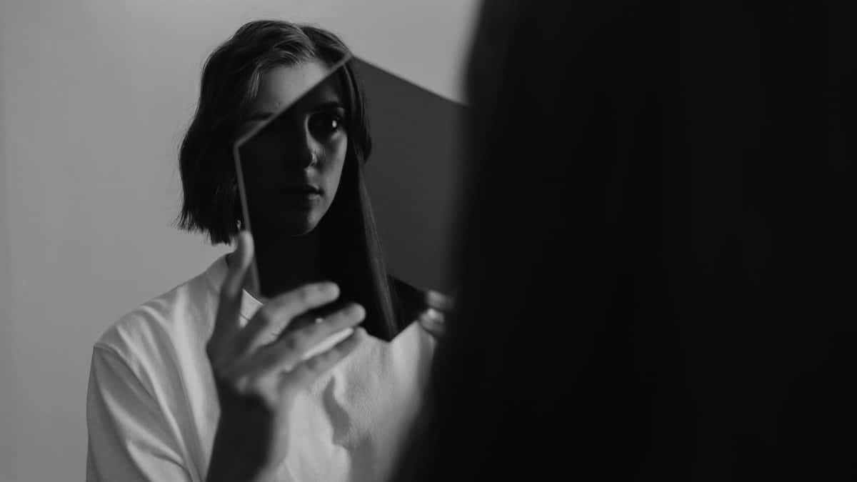 Monochrome image of a woman reflecting on herself in a mirror, evoking introspection.