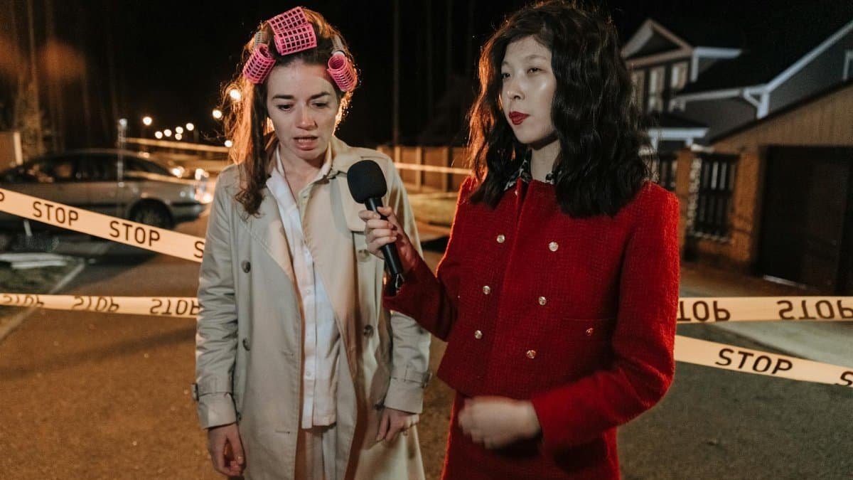 A journalist interviews a woman with curlers at a nighttime crime scene.