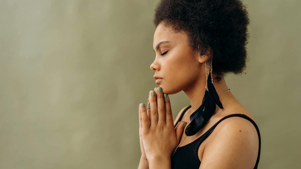 A young woman with afro hair practicing calming meditation indoors.