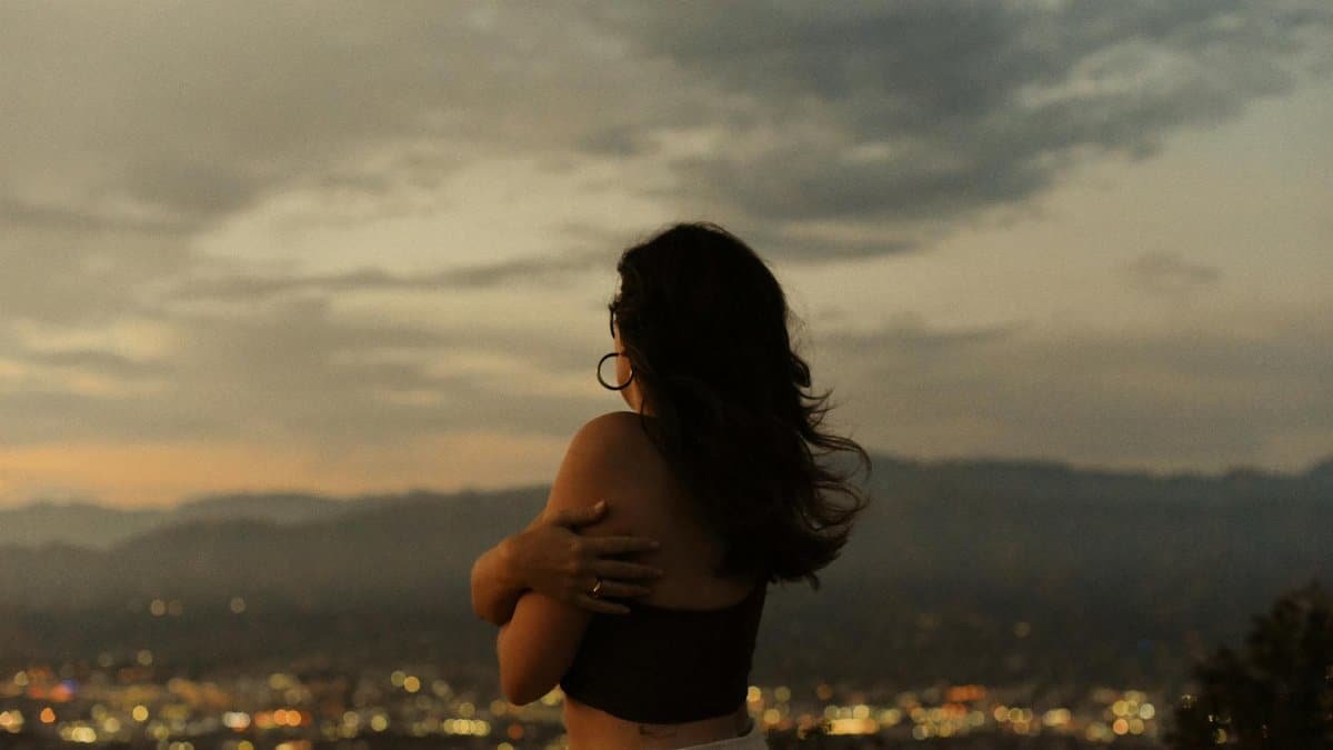 A woman embraces the serene sunset over Los Angeles, blending nature with city lights.
