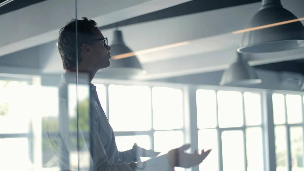 Business professional giving a presentation in a modern office setting through glass.