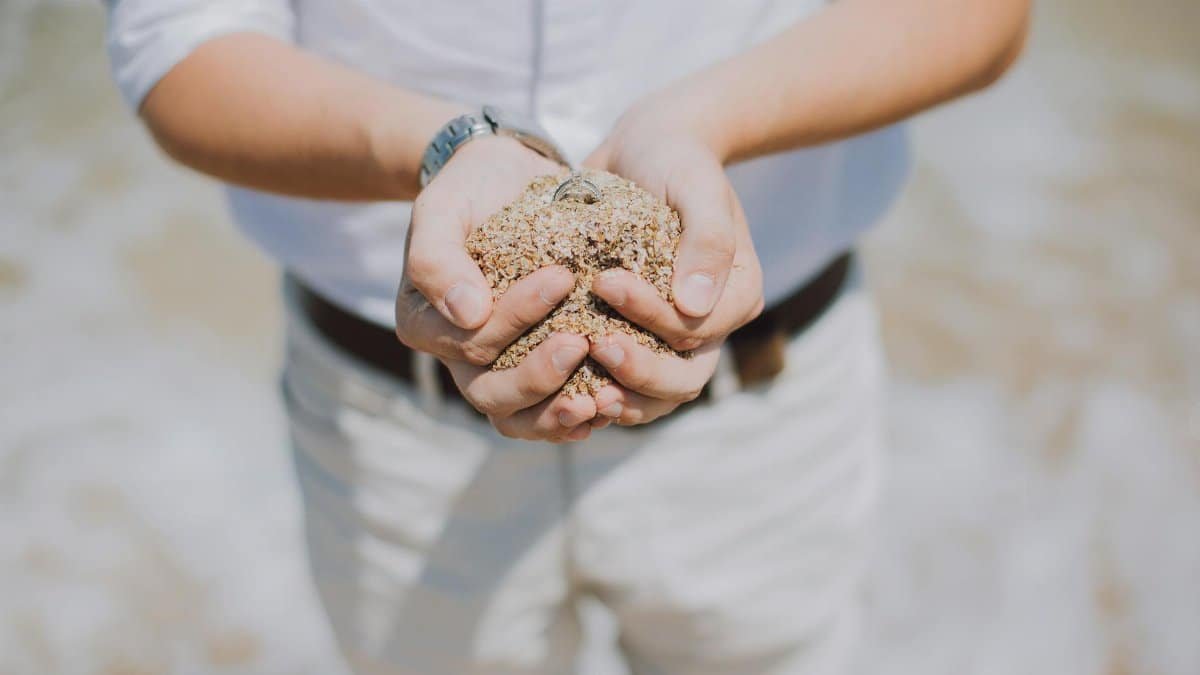 Close-up of a man's hands holding sand and a watch at the beach. Summertime scene.